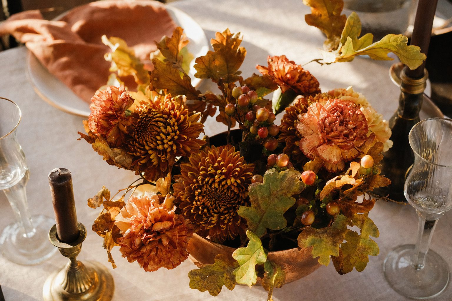 Low autumn centerpiece of bronze mums, rust carnations and berries on a set dining table